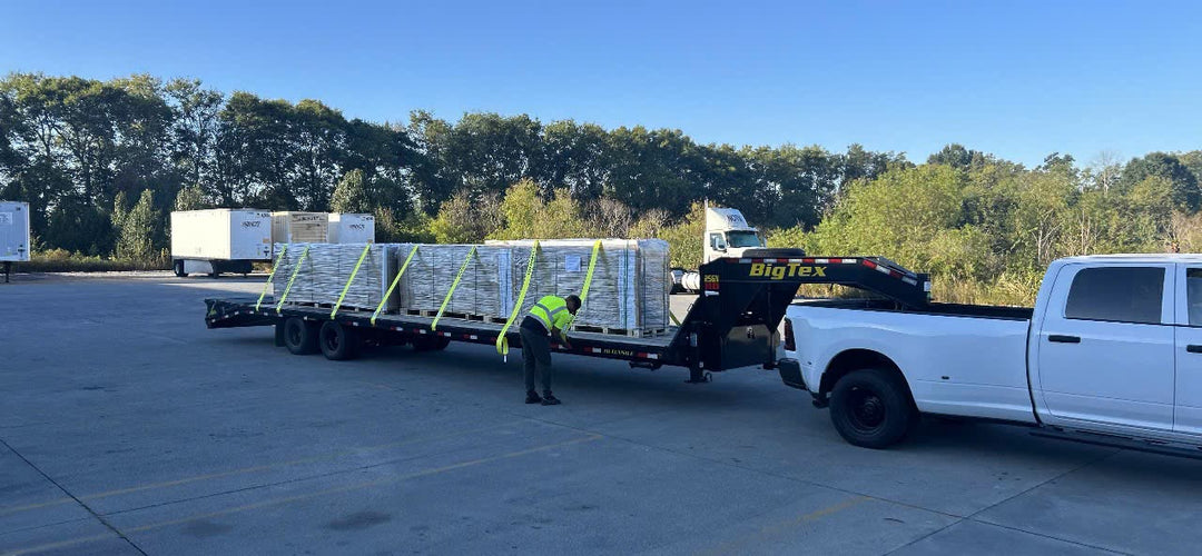 A driver strapping pallets of butcher block tops onto a flatbed trailer